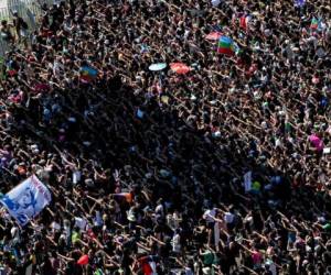 La sombra de la bandera nacional chilena ondeando frente al Palacio Presidencial de La Moneda en Santiago, se proyecta sobre los manifestantes que gesticulan durante una marcha en el Día Internacional de la Mujer, el 8 de marzo de 2020. Foto AFP