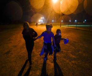 Tres migrantes se toman de las manos mientras corren bajo la lluvia en una zona de detención después de entregarse a las autoridades luego de cruzar la frontera desde México hacia Estados Unidos en Roma, Texas. (AP Foto/Gregory Bull, Archivo)