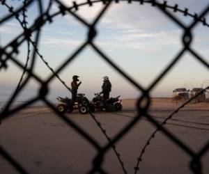 Dos agentes de la Patrulla Fronteriza de Estados Unidos hablando en la playa en San Diego, vistos a través de una cerca desde Tijuana, México. Foto: AP
