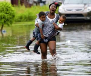 Una mujer llora mientras camina en el agua cargando a dos menores. Foto AP