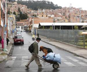 Un hombre cruza la calle empujando una carretilla con su perro montado durante una cuarentena decretada por el gobierno que solo permite a los residentes salir a realizar compras esenciales por las mañanas en un intento por contener la propagación del nuevo coronavirus, en La Paz, Bolivia. Foto: AP.