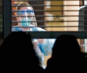 Una trabajadora vestida con una máscara y un traje de protección, vista a través de una ventana en el interior de la habitación de Susan Hailey, de 76 años, quien dio positivo por un nuevo coronavirus, mientras las hijas de la paciente observan desde fuera, el 10 de marzo de 2020, en el Life Care Center en Kirkland, Washington, cerca de Seattle. AP