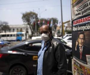 Un hombre usando mascarilla para protegerse del nuevo coronavirus pasa junto a un puesto de periódicos que muestra en primera plana al presidente Martí­n Vizcarra, afuera del Congreso en Lima, Perú. Foto: AP.