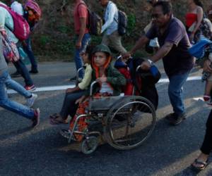 Un migrante, parte de una caravana que se dirige a la frontera entre México y Estados Unidos, empuja la silla de ruedas de un menor por la carretera en Escuintla, Chiapas, México, el sábado 20 de abril de 2019.