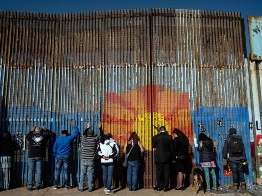 Las personas oran mientras se apoyan en la valla fronteriza México-Estados Unidos, durante la celebración de un servicio religioso en ambos lados de la valla en Playas de Tijuana, estado de Baja California, México, el 3 de febrero de 2019. / AFP / Guillermo Arias.