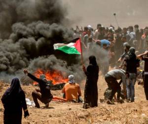 Una mujer palestina sosteniendo su bandera nacional observa los enfrentamientos con las fuerzas israelíes cerca de la frontera entre la franja de Gaza e Israel al este de la ciudad de Gaza.