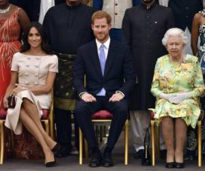 El príncipe Harry, su esposa Meghan Markle (izq) y su abuela, la reina Isabel II, fotografiados durante una ceremonia en el Palacio de Buckingham. Foto: Agencias AP.