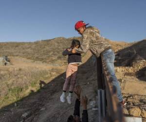 Un migrante hondureño pasa a una niña con su padre después de que brincaron la barda fronteriza para cruzar a San Diego, California, desde Tijuana, México, el jueves 3 de enero de 2019. (AP Foto/Daniel Ochoa de Olza)