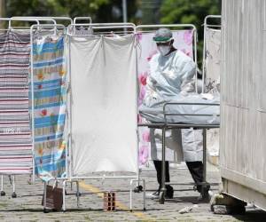 El cuerpo médico de una víctima del coronavirus COVID-19 es trasladado por personal médico en trajes protectores a un área refrigerada del Hospital. Foto: Agencia AFP.