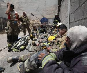 Bajo el sol y con fatiga en sus rostros, elementos del Cuerpo de Bomberos continúan con las labores de rescate para sacar al total del personal que quedó atrapado, luego de que un cerro se desplomara y provocara un incendio que causó pérdidas materiales en una bodega en el anillo periférico.
