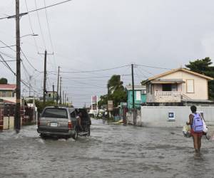 Un vehículo y peatones recorren una calle inundada debido a las fuertes lluvias antes de la llegada del huracán Lisa que ya avanza hacia el oeste de Centroamérica tras dejar lluvias en la zona insular de Honduras.