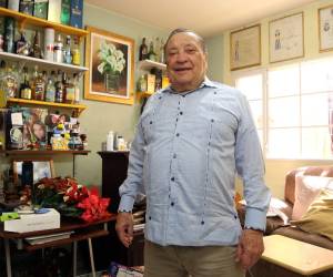 El doctor Augusto Aguilar posando junto a su guaroteca, un espacio donde guarda todas las bebidas que le han regalado en los lugares en los que ha participado como observador electoral.