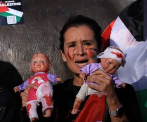 Una mujer sostiene dos muñecos pintados como si estuvieran lastimados, representando a los bebés en Palestina tras los bombardeos de Israel.
