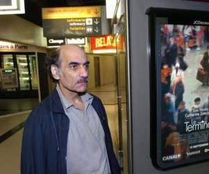 Mehran Karimi Naser junto al poster de la película “La Terminal” de Steven Spielberg inspirada en su vida.