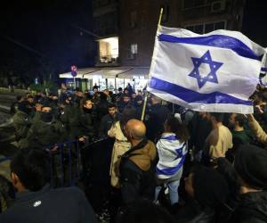 Los manifestantes corean y agitan banderas nacionales durante una manifestación contra las reformas judiciales del gobierno israelí frente a la residencia del primer ministro Benjamin Netanyahu en Jerusalén, el 27 de marzo de 2023.