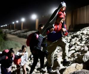 Migrantes que buscan asilo en los Estados Unidos caminan a lo largo de la valla fronteriza en camino a ser procesados por agentes de la Patrulla Fronteriza de los Estados Unidos.