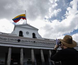 Un turista toma una foto del Palacio Presidencial de Carondelet con la bandera ecuatoriana izada hasta la mitad en honor al asesinado candidato presidencial ecuatoriano Fernando Villavicencio.