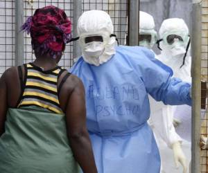 Health workers in protective suits greet a woman who has come to deliver food to relatives at Island Hospital where people suffering from the Ebola virus are being treated in Monrovia on September 30, 2014. Liberia has been hit the hardest by the worst ever outbreak of Ebola, which has killed more than 3,000 people in west Africa. The latest UN data said 1,830 people have died from the killer virus in Liberia so far, and 3,458 people have been infected. AFP PHOTO / PASCAL GUYOT