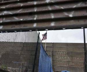 Una bandera nacional de EE. UU. Cuelga de la valla fronteriza entre Estados Unidos y México en Tijuana, Baja California. Agencia AFP.