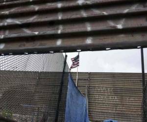Una bandera nacional de EE. UU. Cuelga de la valla fronteriza entre Estados Unidos y México en Tijuana, Baja California. Agencia AFP.