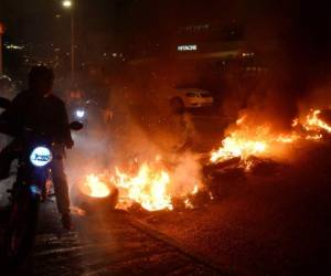 Un motociclista cruza entre las llamas que bloquean una carretera en Tegucigalpa durante un día de protestas. Fotos: AFP.