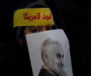 Un niño se asoma desde detrás de una imagen de la Guardia Revolucionaria iraní asesinada, general Qassem Soleimani, mientras los partidarios del líder de Hezbolá, Sayyed Hassan Nasrallah, se reúnen para su discurso televisado en un suburbio al sur de Beirut, Líbano, el domingo 5 de enero de 2020 tras el ataque aéreo estadounidense en Iraq que mató a Soleimani. La diadema dice: 'muerte a América'. (Foto AP / Maya Alleruzzo)