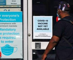 Un individuo pasa junto a una tienda de Walgreens que tiene un cartel que dice que todavia no hay disponible una vacuna contra el COVID-19 y otro que recomienda el uso de barbijos en Long Beach, California, el 2 de diciembre del 2020. (AP Photo/Ashley Landis, File).