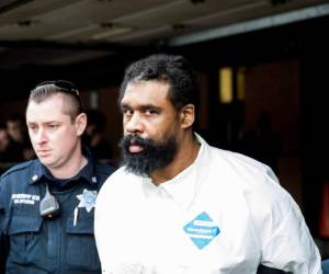 Agentes escoltan a Grafton Thomas desde el ayuntamiento a un vehículo de la policía, el domingo 29 de diciembre de 2019, en Ramapo, Nueva York. Thomas está acusado de apuñalar a varias personas en casa de un rabino al norte de la ciudad de Nueva York. (AP Foto/Julius Constantine Motal)