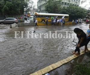 Una mujer junto a una menor intenta cruzar la calle inundada por las aguas producto de las lluvias que cayeron las tarde de este domingo en la capital de Honduras. Foto: David Romero/ EL HERALDO
