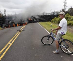 En esta fotografía de archivo del 5 de mayo de 2018, Sam Knox, habitante de Leilani Estates, observa una franja de lava que cruza un camino en Pahoa, Hawai.