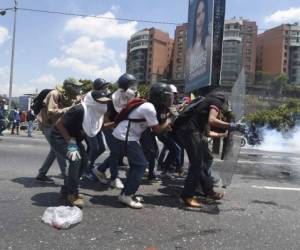 Un grupo de jóvenes se protege de los proyectiles de goma lanzados por las fuerzas del orden durante la protesta de la oposición de Venezuela, foto: Agencia AFP.