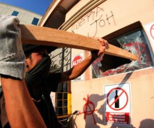 Con palo en mano y guantes un manifestante rompe la ventana de una caseta de seguridad en el edificio donde funcionaba la Casa Presidencial. (Foto: AFP/ El Heraldo Honduras/ Noticias Honduras hoy)