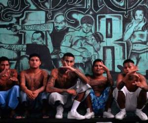 Miembros de la pandilla barrio 18 hacen señas en un muro pintado con su símbolo.