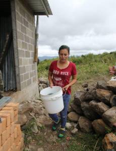 Liliana Aguiluz traslada agua en un balde plástico hacia su pila improvisada con piedras en las afueras de su vivienda, una escena que se repite en las periferias de la capital.