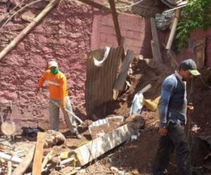 Miembros de Copeco limpian los escombros de una pared que cedió por las fuertes lluvias en La Trinidad.