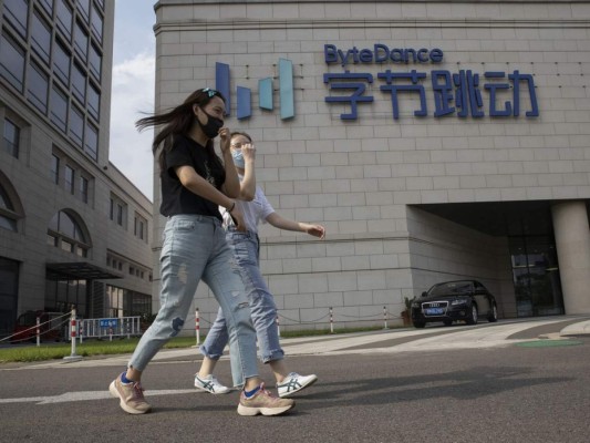 Un par de mujeres que llevan mascarillas para impedir la propagación del coronavirus pasan frente a la sede de ByteDance en Beijing, China, el viernes 7 de agosto de 2020. (AP foto/Ng Han Guan).
