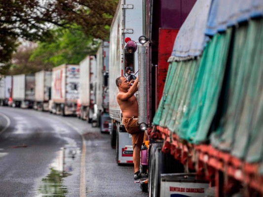 A la espera de una solución, los conductores se las ingenian para sobrevivir: duermen en los camiones entre zancudos, con riesgo de contraer dengue, compran galones de agua a los lugareños para beber y bañarse y se alimentan de comidas callejeras. AFP.