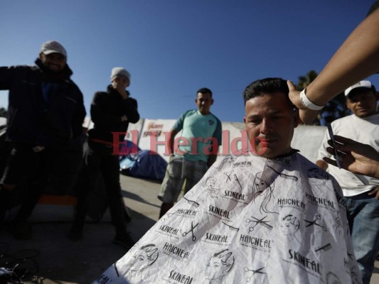 En esta imagen del 3 de diciembre de 2018, el peluquero hondureño Daniel Villafranca, de 19 años de edad, le corta el cabello a otro inmigrante, Juan Francisco Medrano, mientras otros clientes esperan su turno dentro de la exsala de conciertos Barretal, que actualmente está habilitada como refugio para más de 2,000 inmigrantes, en Tijuana, México. (AP Foto/Rebecca Blackwell)