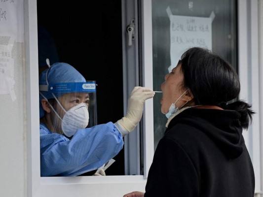 Un trabajador de la salud toma una muestra de un hisopo de una mujer para ser examinada por el coronavirus Covid-19 en Beijing el 28 de octubre de 2021. Foto: AFP