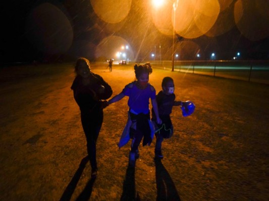 Tres migrantes se toman de las manos mientras corren bajo la lluvia en una zona de detención después de entregarse a las autoridades luego de cruzar la frontera desde México hacia Estados Unidos en Roma, Texas. (AP Foto/Gregory Bull, Archivo)