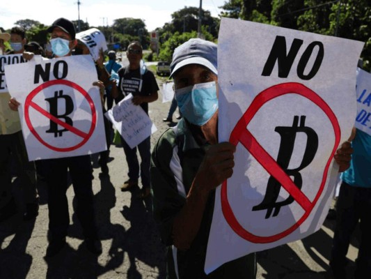 Agricultores sostienen carteles con mensajes contra la adopción del bitcoin como moneda de curso legal durante una protesta a lo largo de la Carretera Panamericana en San Vicente, El Salvador, el martes 7 de septiembre de 2021. (AP Foto/Salvador Meléndez).