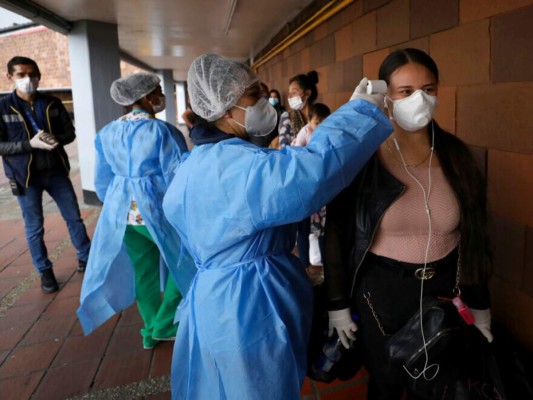 Una enfermera toma la temperatura de una mujer, afuera de la terminal principal de autobuses en Bogotá, Colombia, el martes 24 de marzo de 2020. El gobierno anunció un cierre nacional a partir del martes para combatir la propagación del nuevo coronavirus, imponiendo restricciones estrictas a los movimientos de los residentes, pero enfatizó que garantizará la continuación de la agricultura local y la distribución de alimentos. (Foto AP / Fernando Vergara)