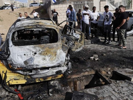 Onlookers gather around charred vehicles hit by rockets launched by Hamas militants from the Gaza Strip in the southern Israeli city of Ashkelon on the border with the Palestinian coastal enclave on May 16, 2021. (Photo by JACK GUEZ / AFP)