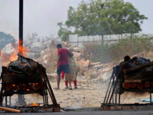 Familiares de víctimas del COVID-19 se marchan mientras sus piras funerarias arden en un crematorio al aire libre en una cantera de granito. Foto: AP