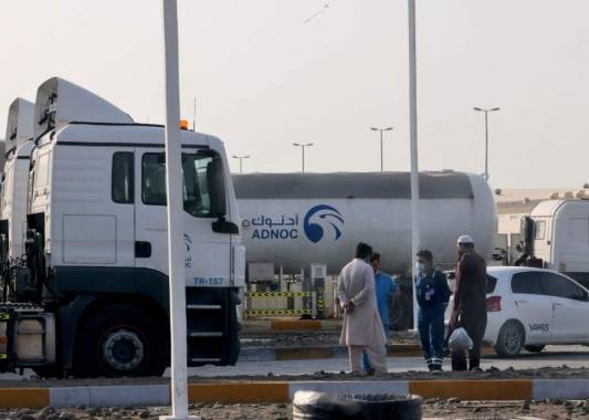 Los hombres se paran frente a una instalación de almacenamiento del gigante petrolero ADNOC en la capital de los Emiratos Árabes Unidos, Abu Dhabi, el 17 de enero de 2022. Foto: AFP