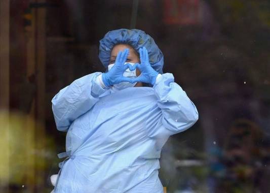 Un trabajador de salud forma un corazón a través de una ventana en un centro médico. Foto: AFP.