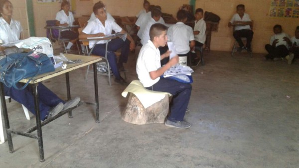 Alumnos reciben clases sentados sobre llantas y troncos de árboles