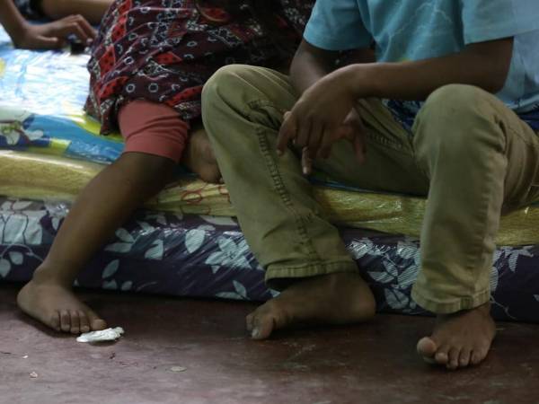 Con sus pies descalzos y sentados sobre colchonetas en el piso, varios menores esperan junto a sus familias el momento de regresar a sus casas, tras tener que ser albergadas en el centro comunal de colonia Ramón Amaya Amador por las fuertes lluvias.