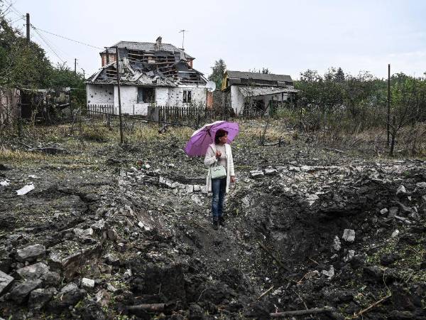 Una mujer se para frente a una casa destruida en medio de la invasión rusa de Ucrania.