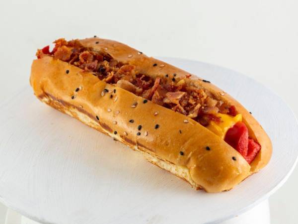 El hot dog con tocino y cebolla caramelizada estilo estadio, una salchicha sobre un pan suave que no necesita presentación.